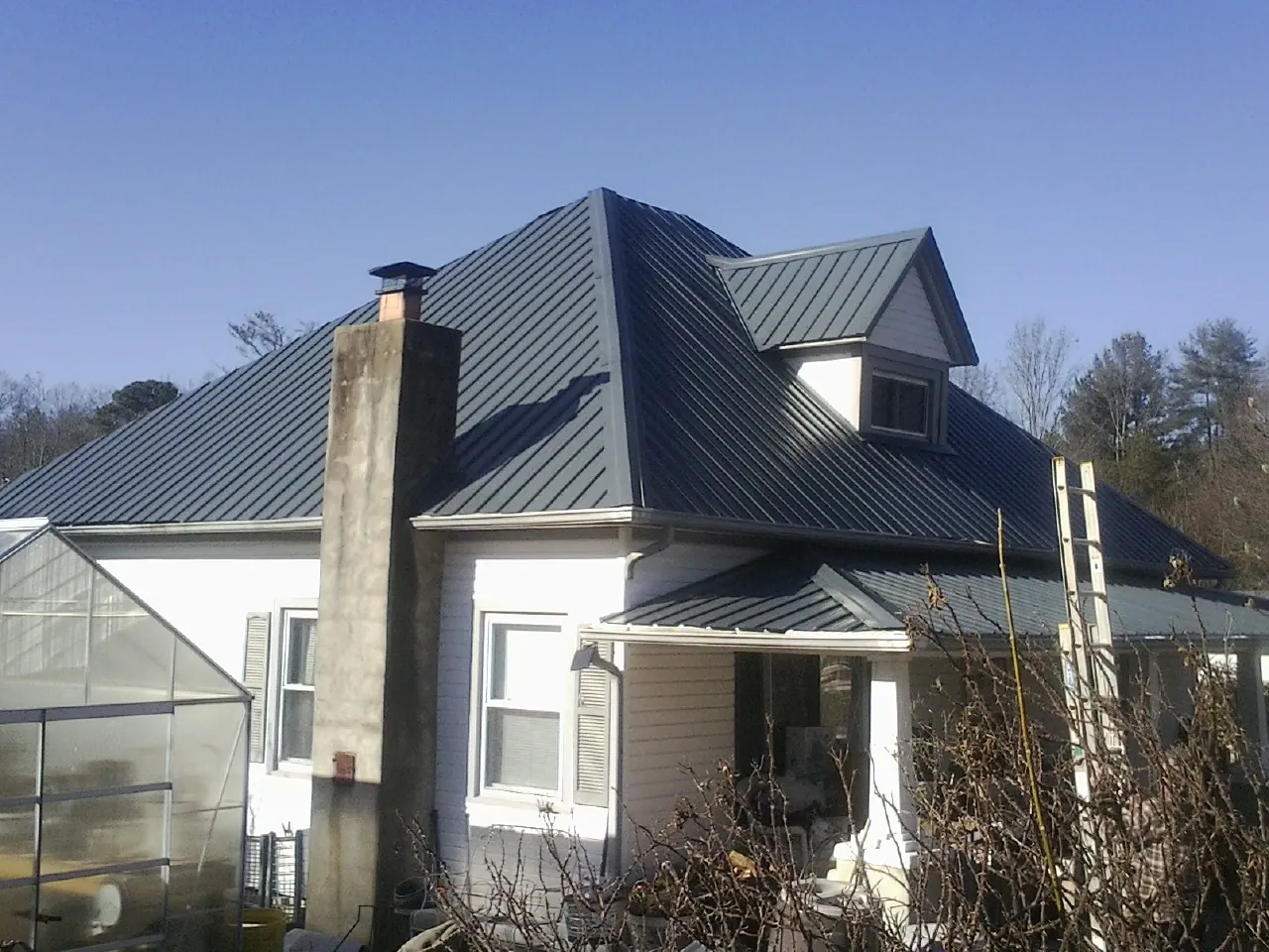 Dark blue standing seam metal roof on a white farmhouse with dormer — Slate & Tile Roof Repair by Roofing Brothers in Haines
