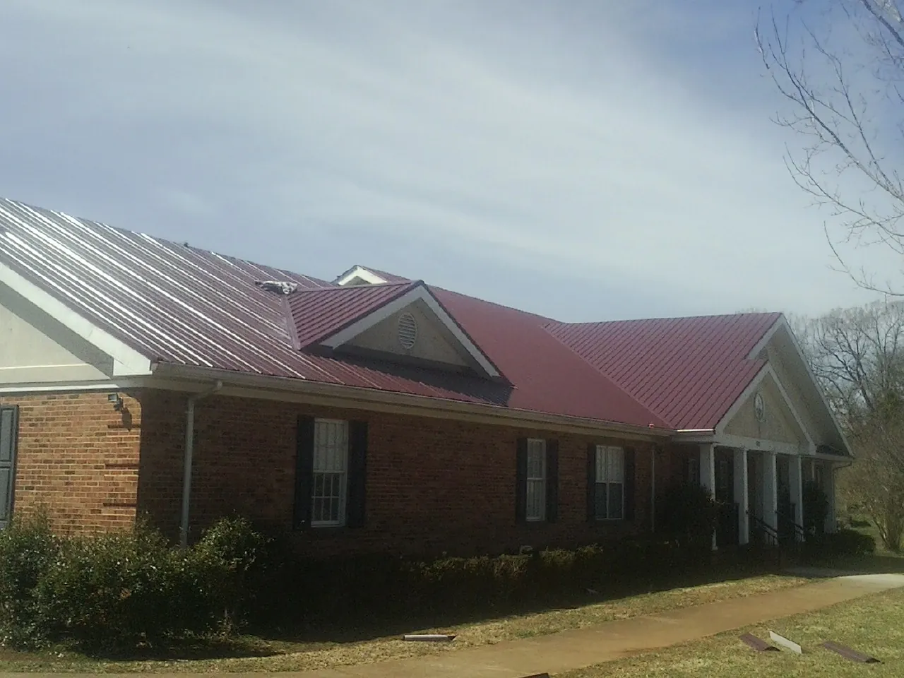 Red metal roof with gabled entries on a long brick building, from a Hail Damage Roof Repair job in Haines