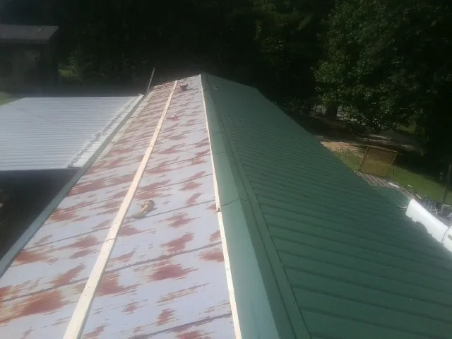 Old rusted panels beside newly installed green metal roofing — Wind Damage Roof Repair by Roofing Brothers in Haines