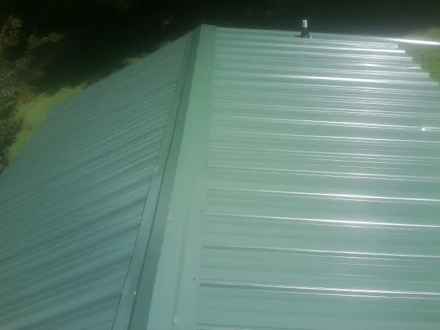 New green metal panels meeting at the ridge of a roof — Flat Roof Repair work by our crew in Haines