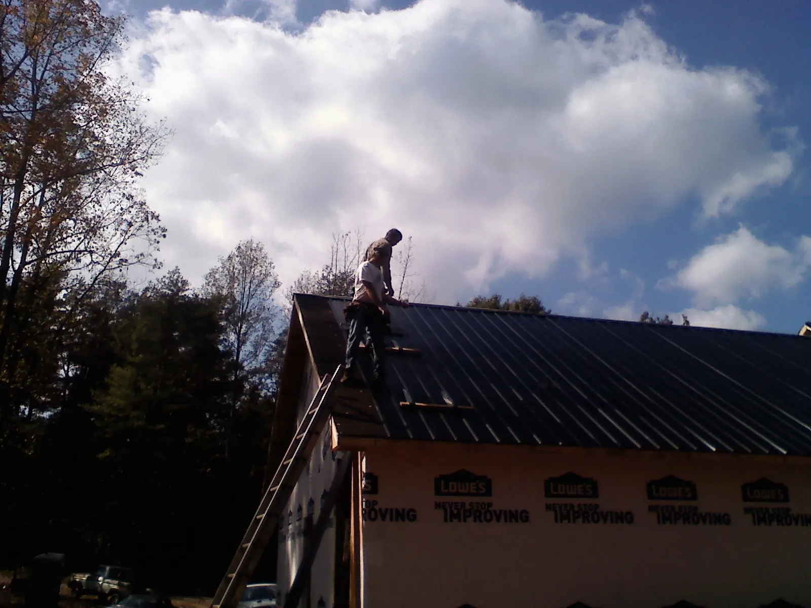 Roofer fastening dark metal panels high against a cloudy sky, from a Roof Inspection job in Haines