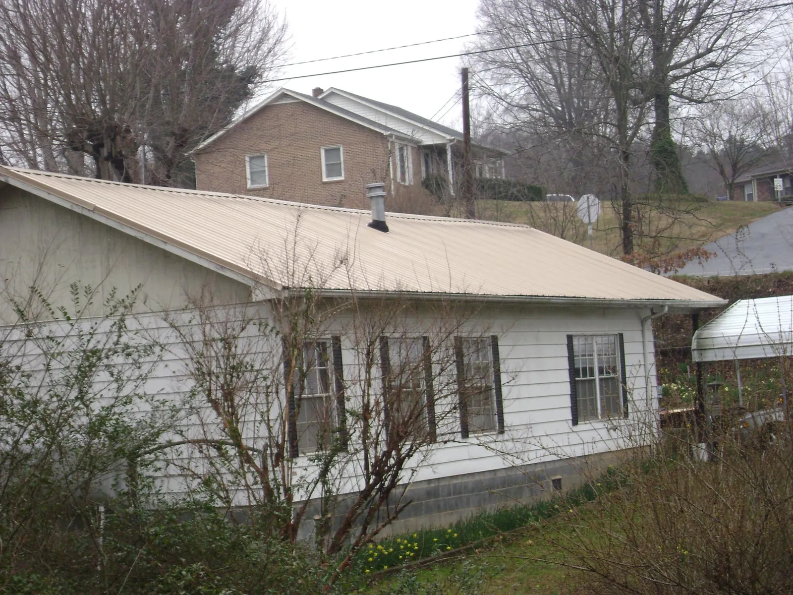 Tan metal roof on a white sided house set into a hillside — Commercial Roofing by Roofing Brothers in Haines