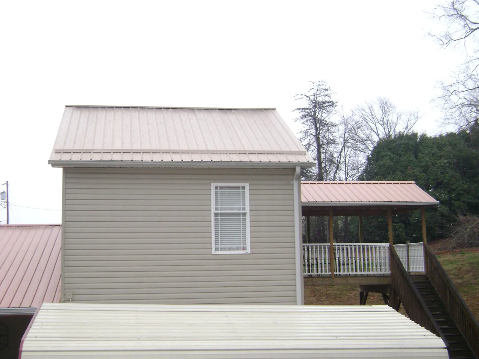 Tan metal roofs on a two story addition and attached porch, from a Roof Replacement job in Haines